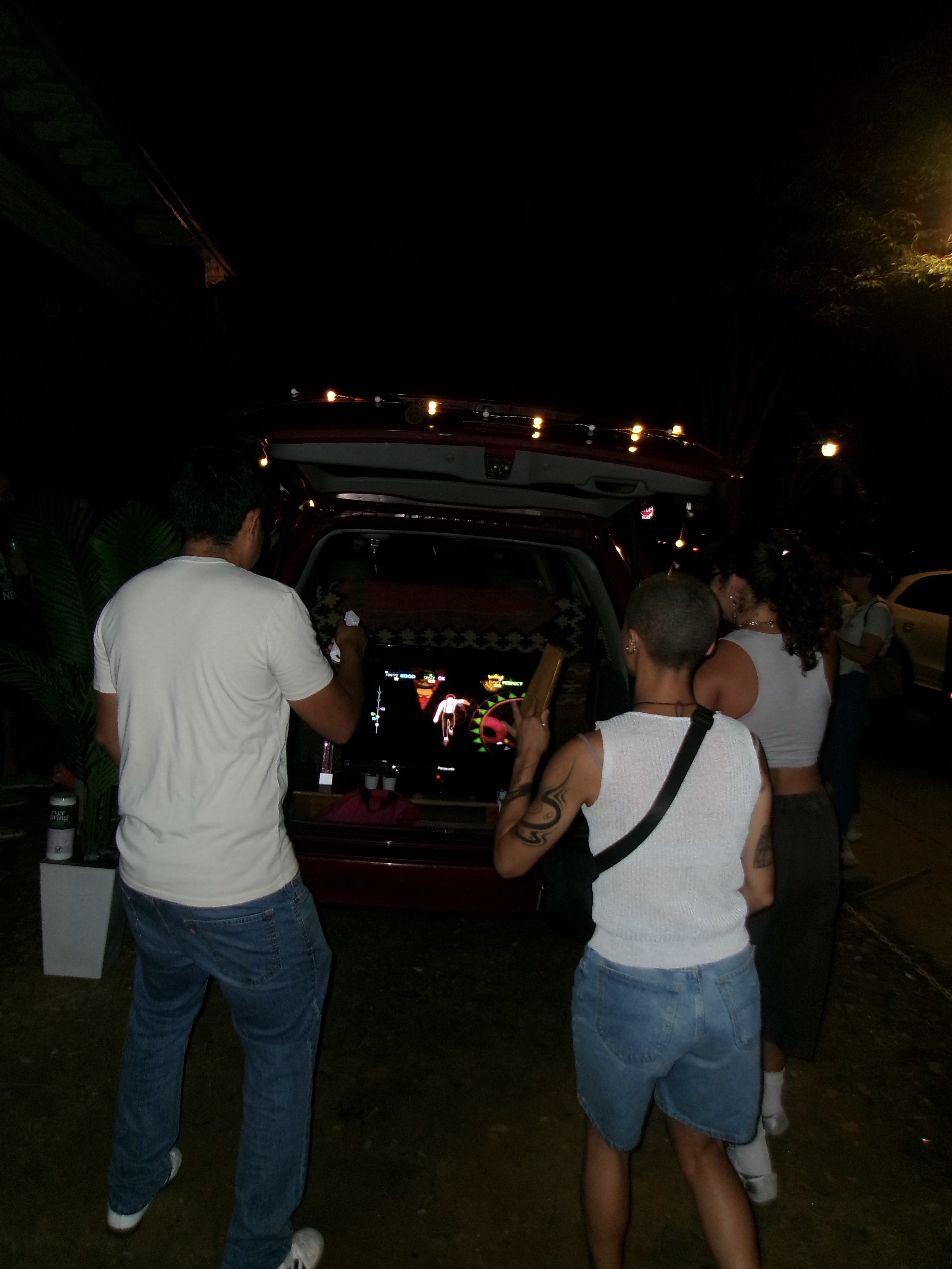 Friends playing Just Dance at the open back of the Reset minivan under string lights