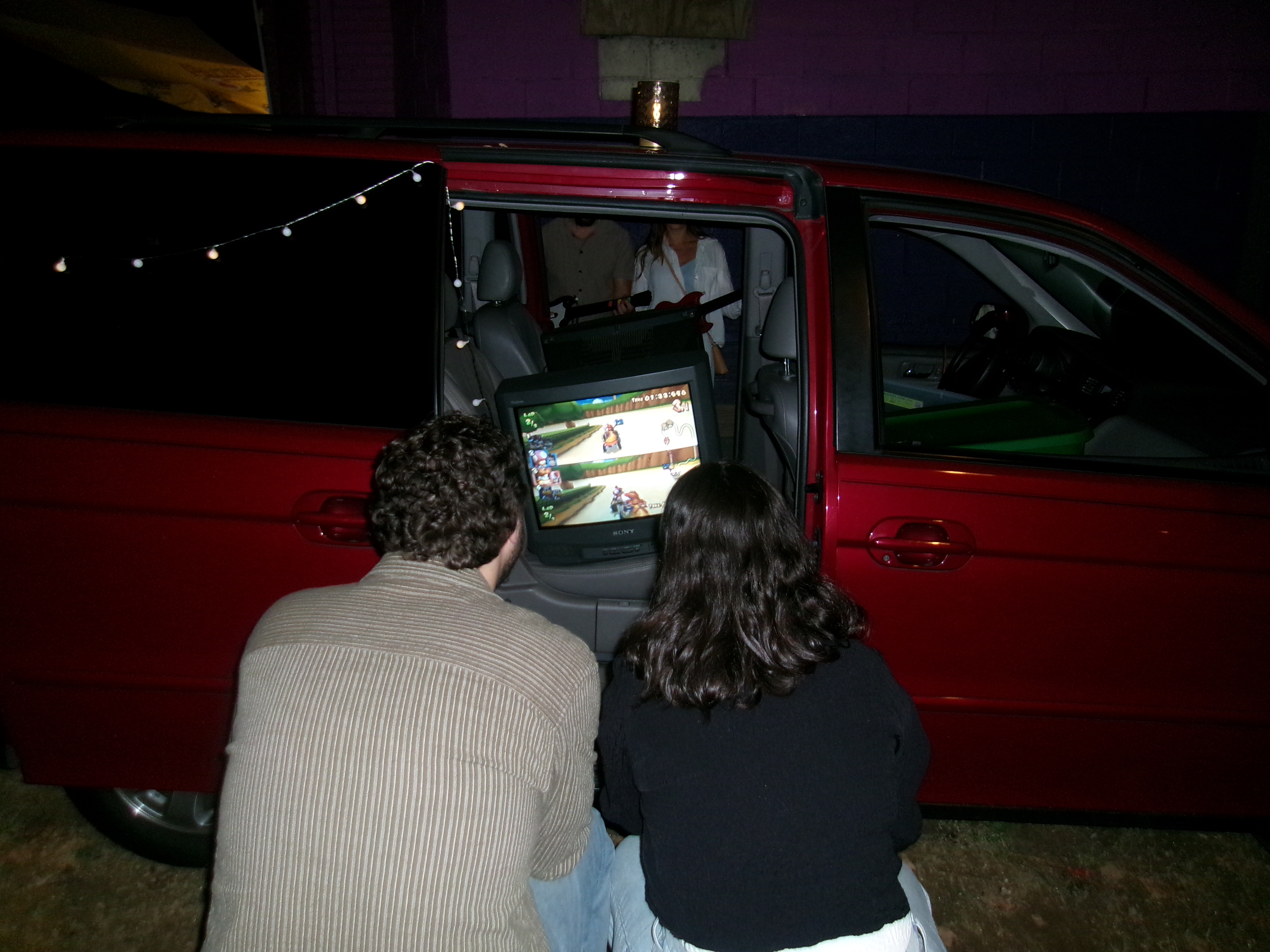 Two friends playing Mario Kart on a CRT television in the red Reset minivan